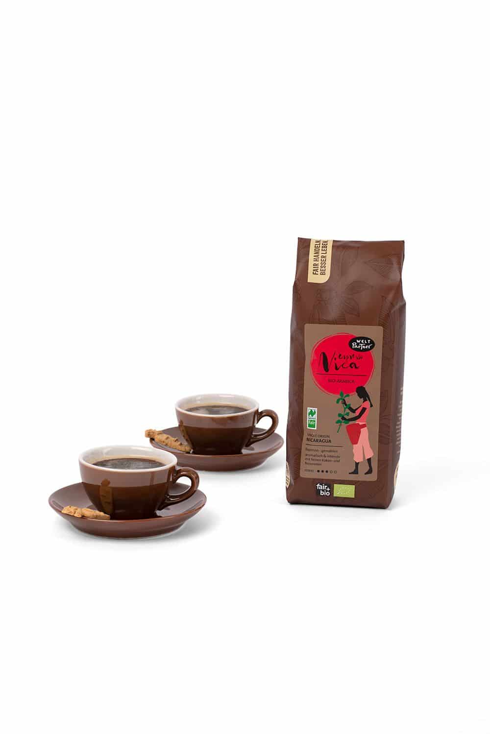 Espresso Nica gemahlen 250 g Espresso Nica in brauner 250g Packung neben zwei braunen Tassen mit Untertellern