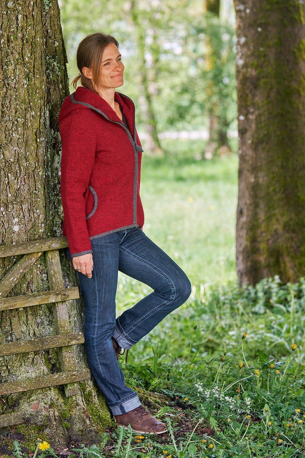 Frau lehnt mit roter Jacke aus einem Strickwalk mit bio Wolle (kbT) vom Finkhof an einem Baum