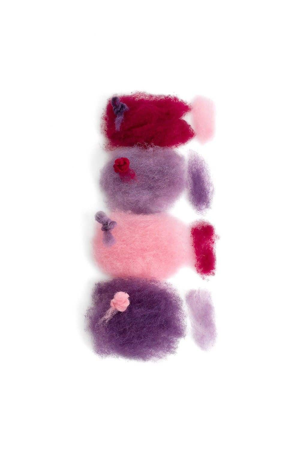 lose lila/ rote Filzwolle auf weißem Untergrund aus der Finkhof Märchenwollepackung aus bio Wolle (kbT)