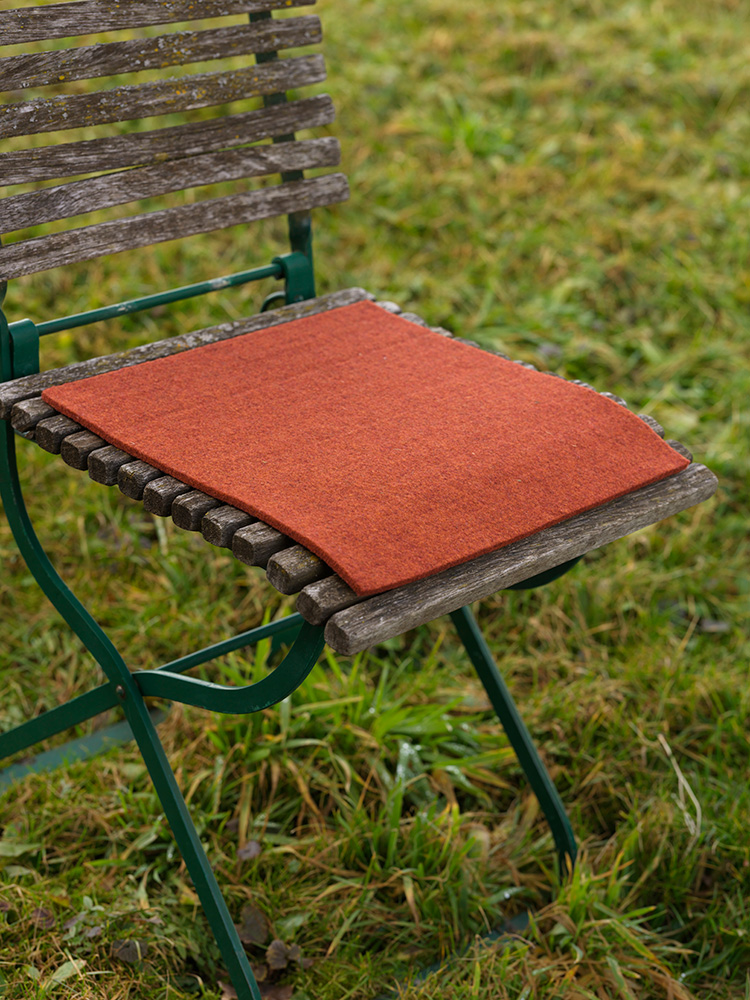 orange eckige Finkhof Sitzauflage aus bio Wolle (kbT) auf einem Gartenstuhl