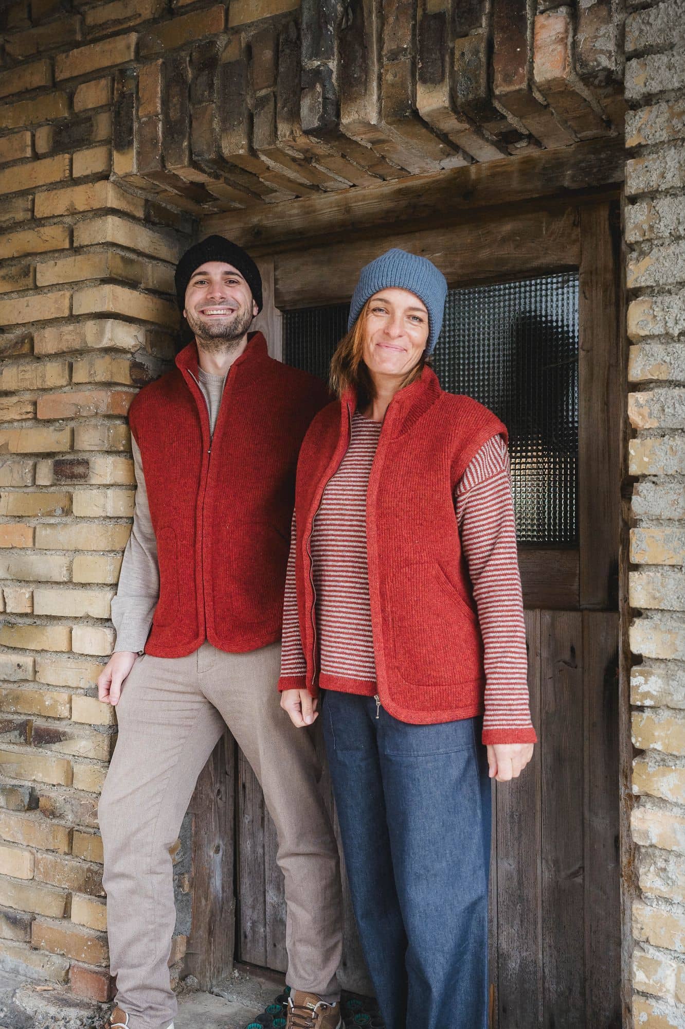 Finkhof-Wollwalkweste gefärbt siena Gr. M Mann und Frau tragen Mützen und rote Wollwalkwesten ohne Ärmel aus bio Wolle (kbT) vom Finkhof