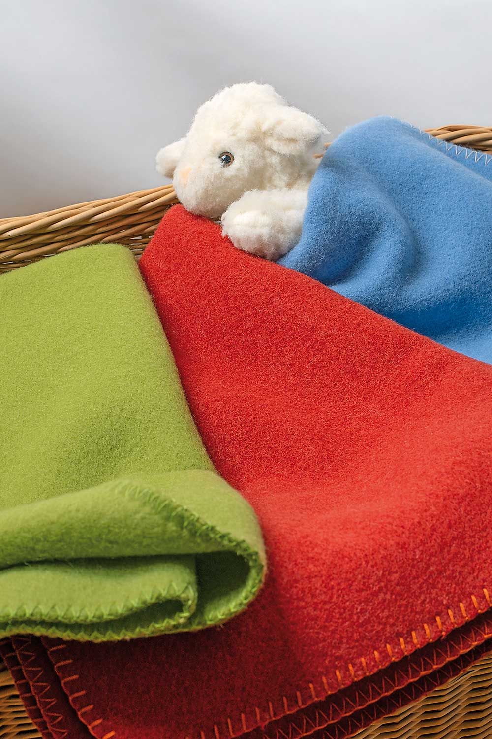Wolldecke Malin Kinder Wolldecke Malin vom Finkhof für Kinder aus bio Wolle (kbT) in rot, blau und grün in Korb mit Plüschschaf