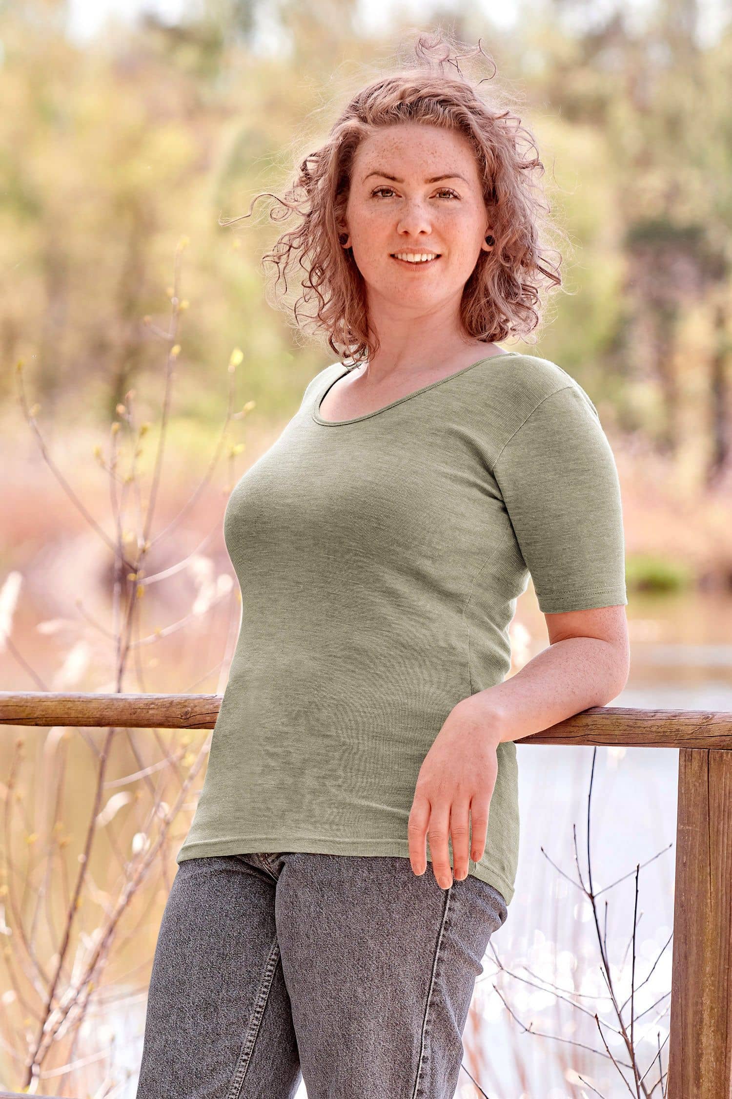 Frau mit Jeans lehnt an Geländer und trägt ein grünes Kurzarmshirt aus bio Wolle (kbT), bio Baumwolle (kbA) und Seide