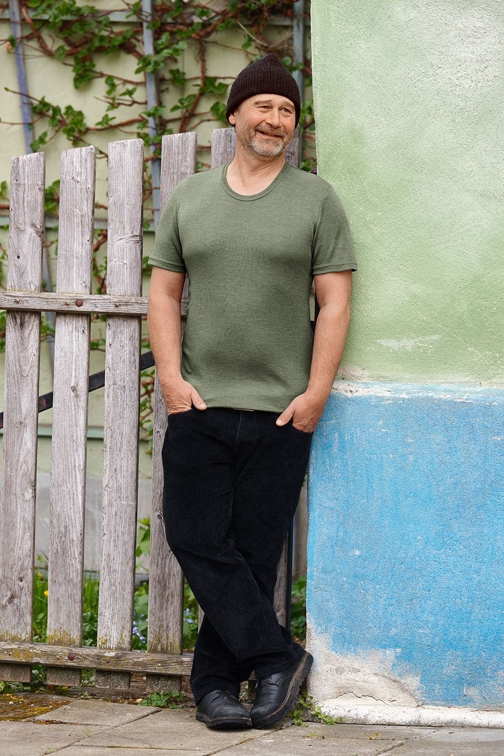 Mann mit Jeans und Mütze lehnt an Wand und trägt grünes Kurzarmshirt aus bio Wolle (kbT) und Seide