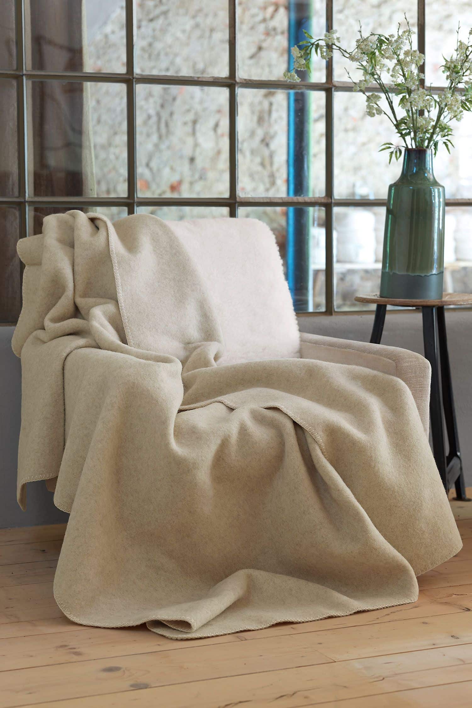 beige Wolldecke aus bio Wolle (kbT) vom Coburger Fuchsschaf vom Finkhof liegt auf beigem Sessel