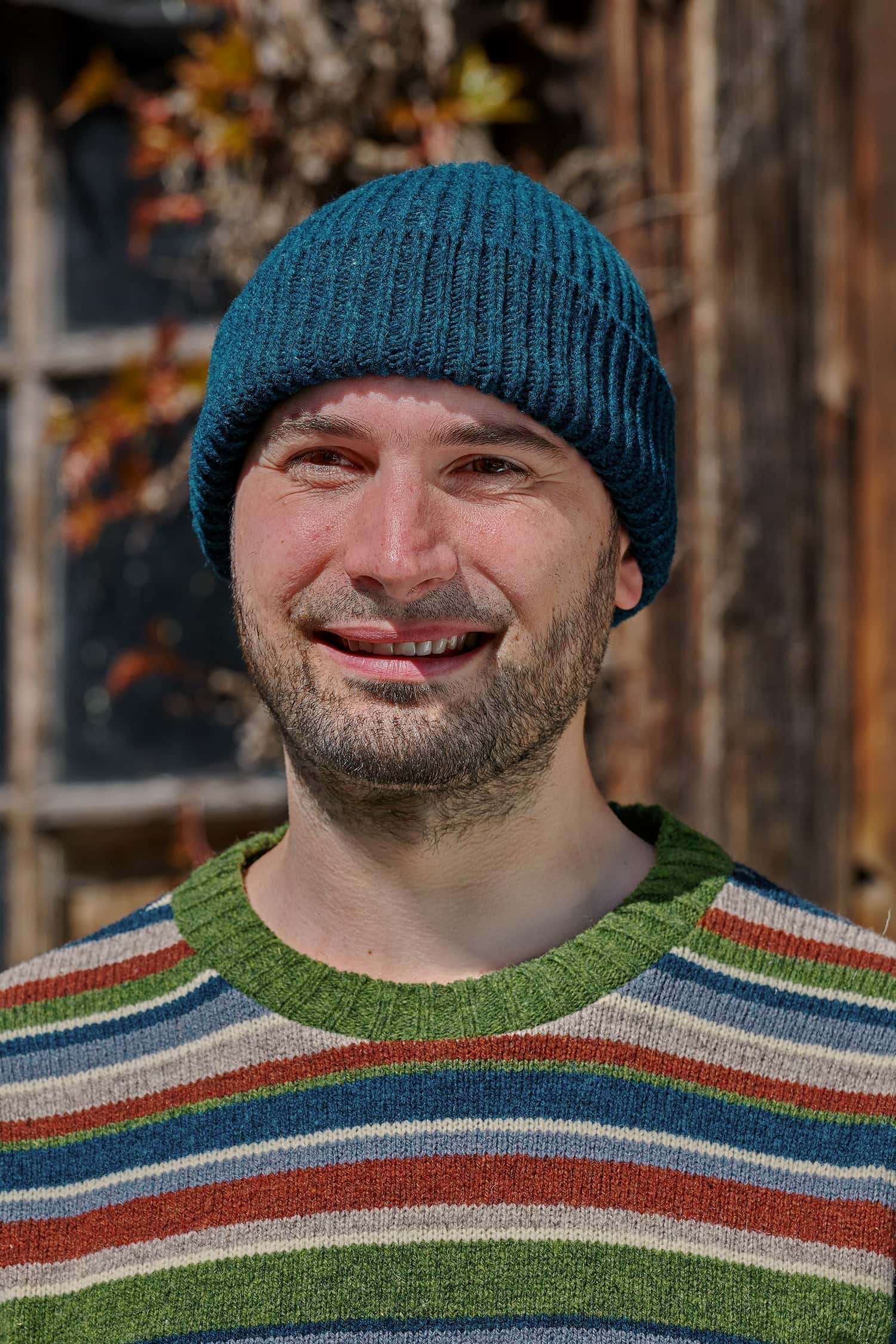 Mann trägt einen bunt gestreiften Strickpullover und eine seeblaue Fischermütze aus Bio-Wolle vom Finkhof