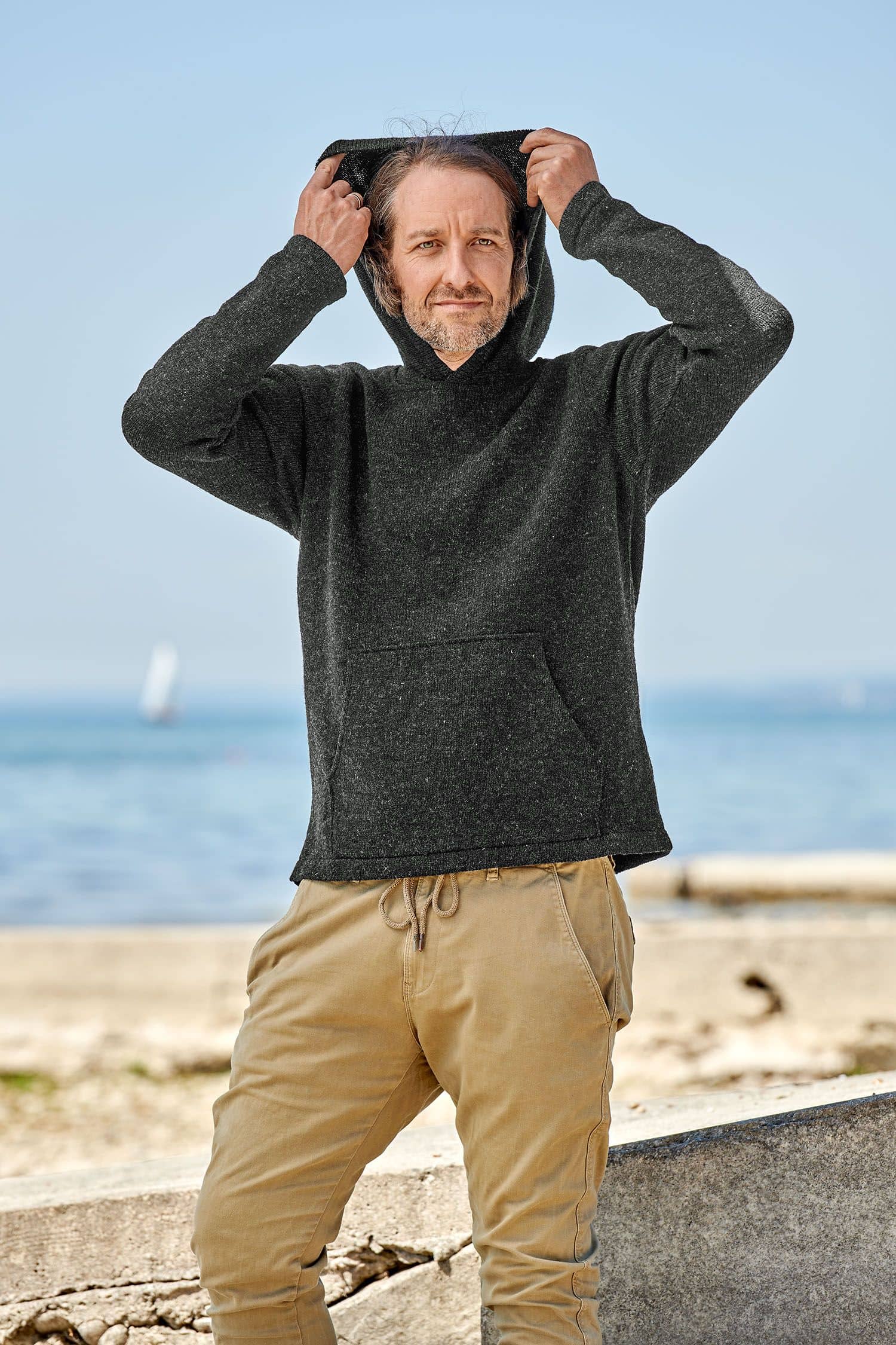 Mann setzt sich Kapuze des anthrazitfarbenen Kapuzenpullis aus bio Merinowolle (kbT) vom Finkhof auf