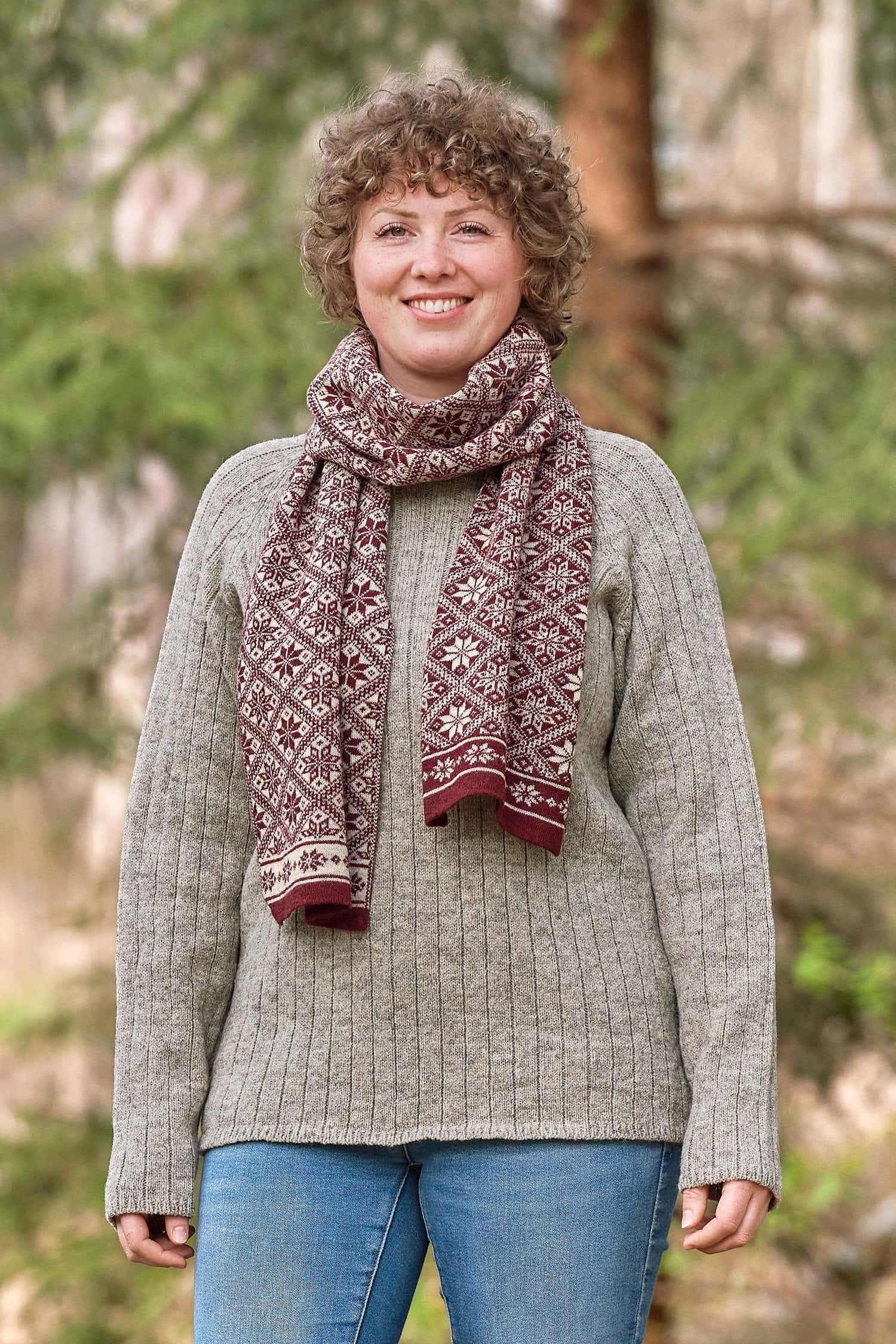 Frau mit grauem Strickpulli trägt roten Schal mit winterlichem Muster aus bio Wolle (kbT)