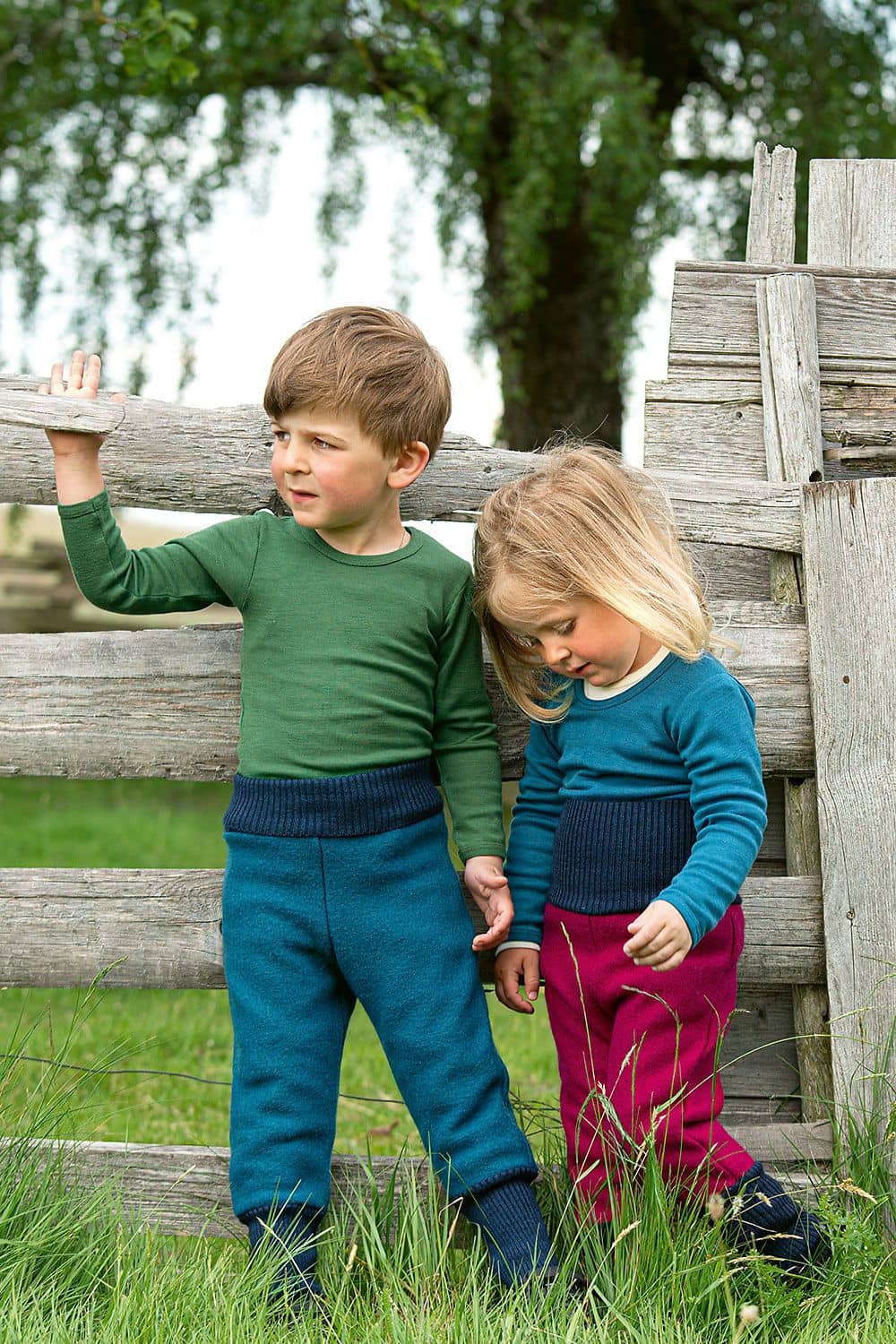 Kinder-Walkhose Kinder vor Holzzaun tragen Finkhof Walkhose aus bio Wolle (kbT) in fuchsia und blau mit einfarbigen Shirts
