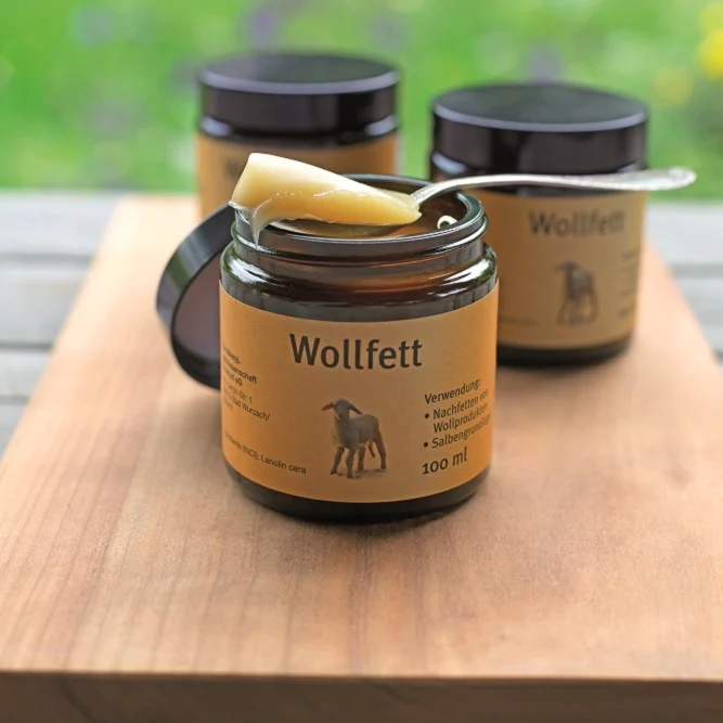 Wollfett geöffnet mit Löffel obendrauf auf einem Holzbrett und Gläschen dahinter
