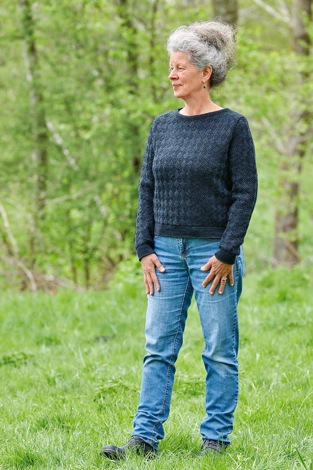 Frau steht auf Wiese und trägt blauen Pullover aus bio Wolle (kbT)