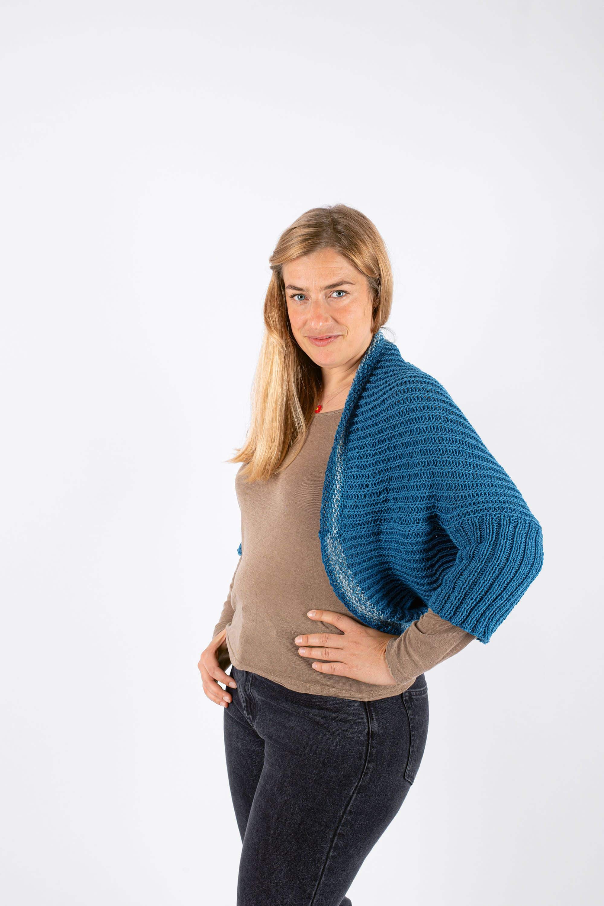 Frau mit blonden Haaren und braunem Shirt hat sich blauen Strickseelenwärmer um Schultern gelegt