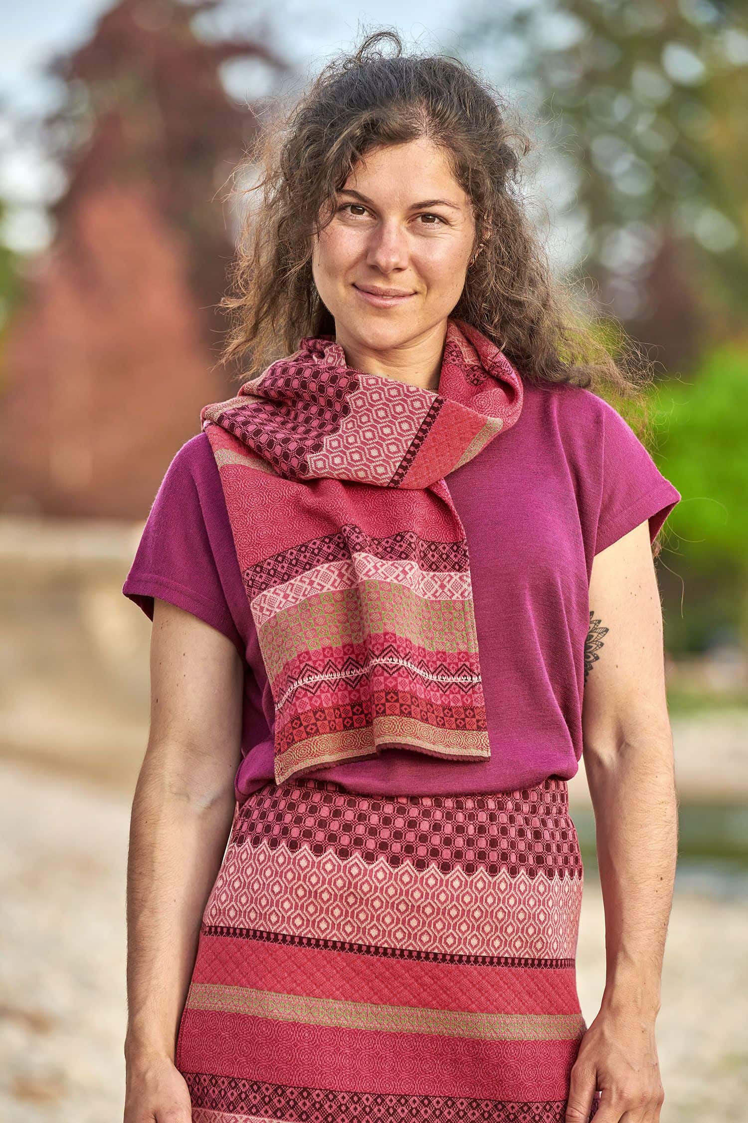 Frau trägt gemusterten Strickschal aus bio Baumwolle (kbA) in beere und pink, einen Rock und ein Shirt