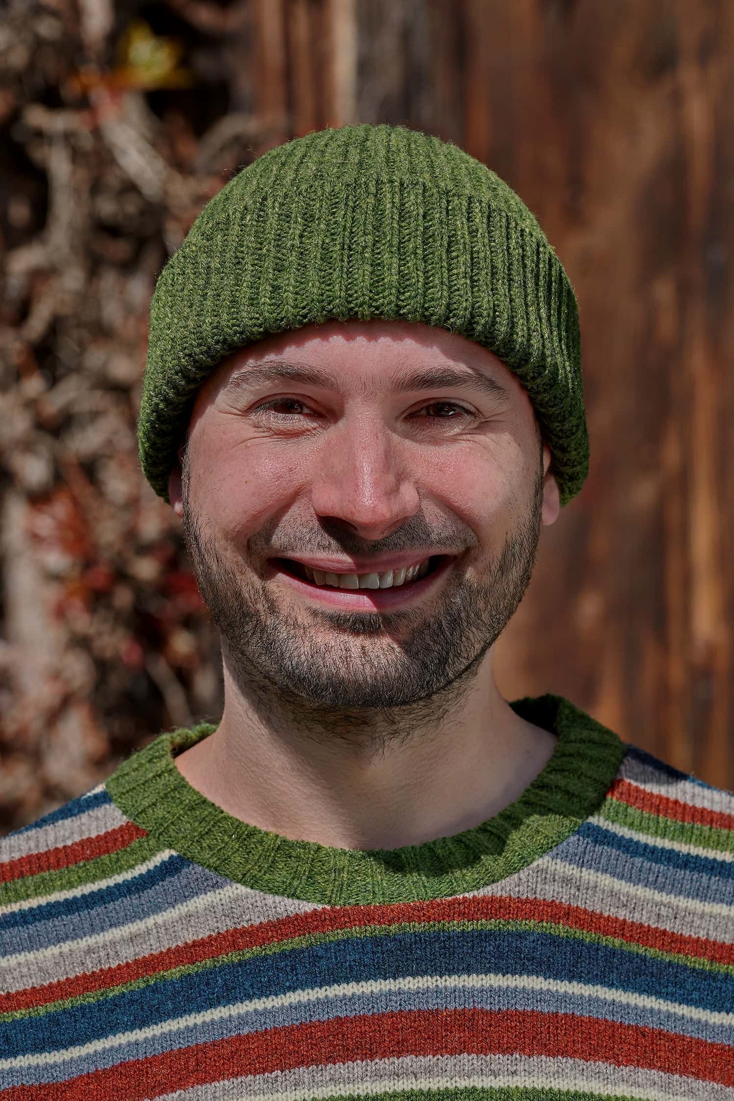 Mann trägt einen bunt gestreiften Strickpullover und eine grüne Fischermütze aus Bio-Wolle vom Finkhof