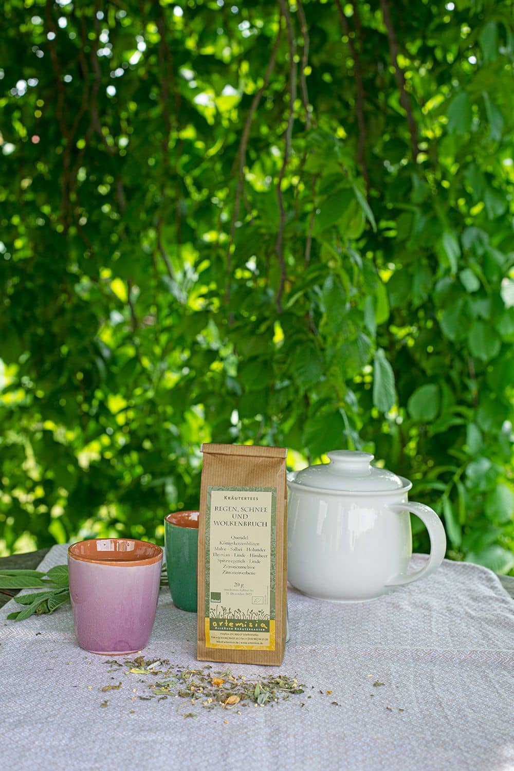 Regen, Schnee und Wolkenbruch - Tee Regen, Schnee und Wolkenbruch Tee in 20g Beutel mit Kräutern, Teekanne und Teebechern unter einem Baum