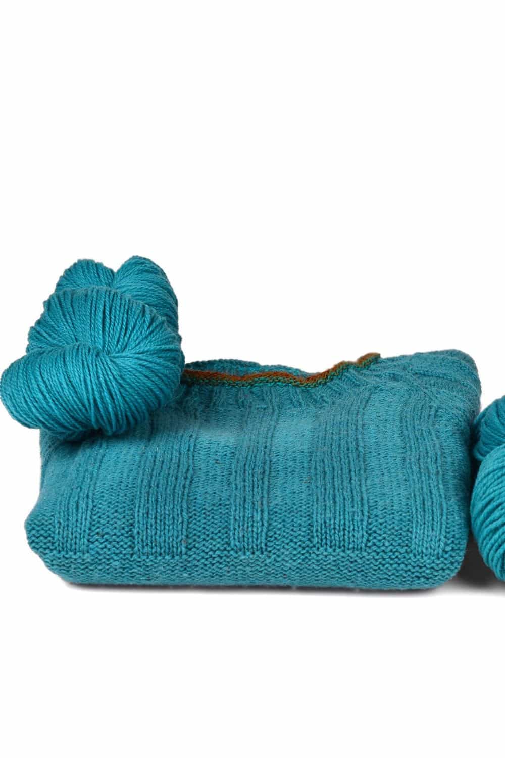 dünne petrolblaue Finkhof Merinowolle aus bio Wolle (kbT) mit Strickpulli darunter, weißer Untergrund