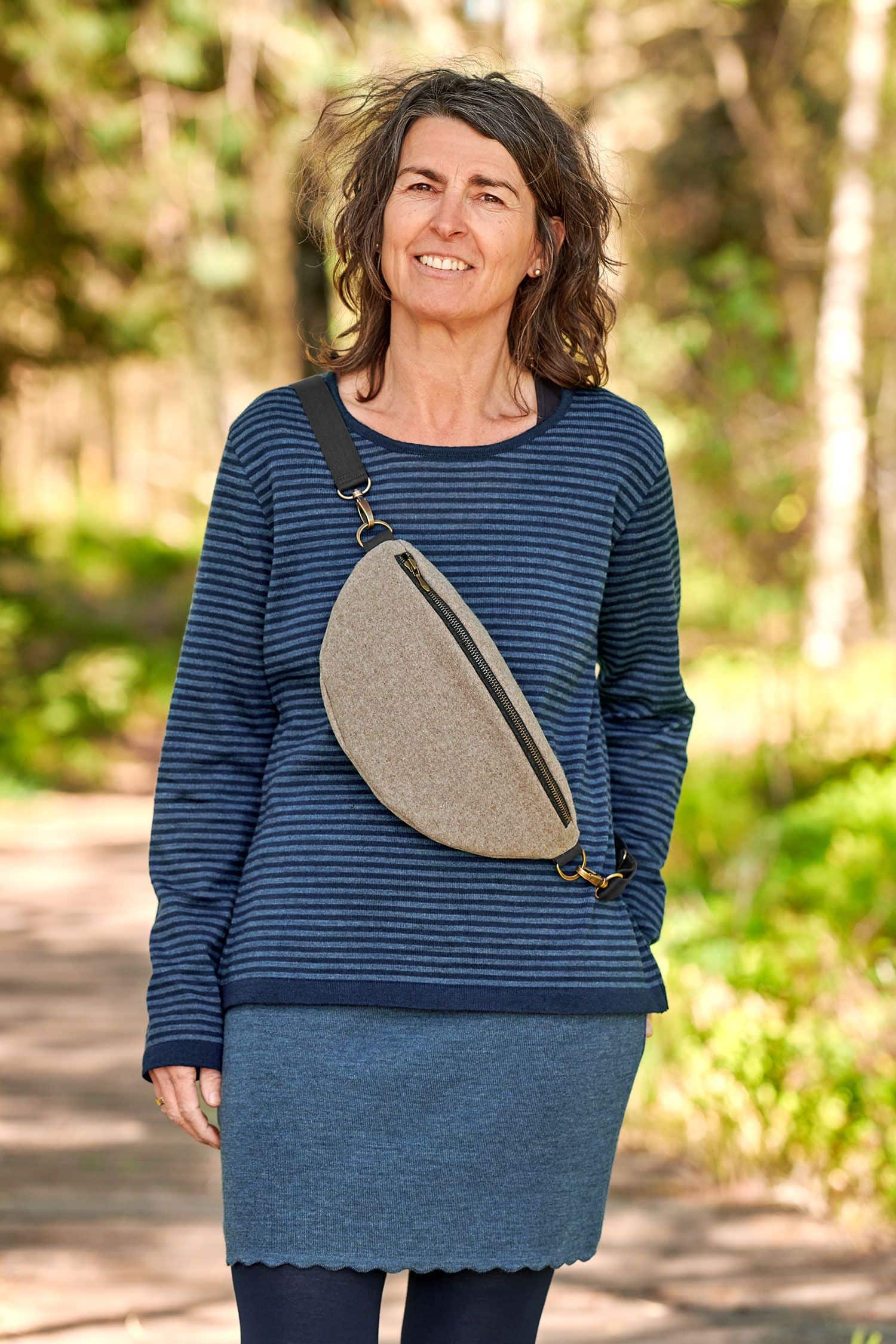 Frau mit blauem Streifenpulli trägt eine beige Bauchtasche aus Loden (Webstoff aus Schurwolle) vom Finkhof