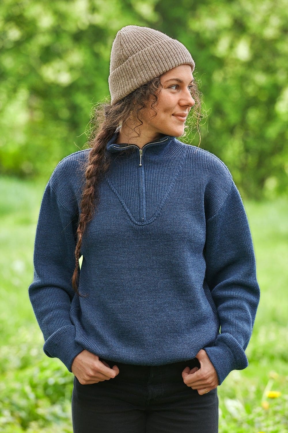 Frau mit blauem Troyer und Zopf trägt graue Finkhof Mütze aus bio Wolle (kbT)