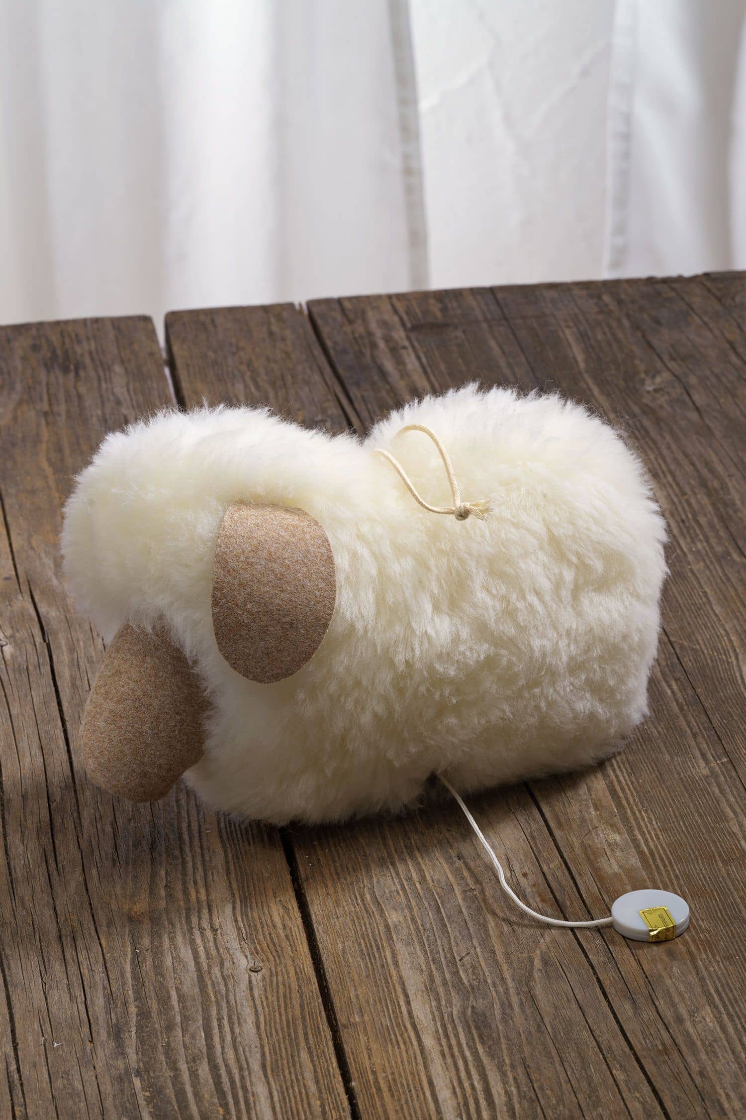 weiße Spieluhr in Schafform, aus bio Wolle und pflanzlich gegerbtem Schaffell auf braunem Holzboden