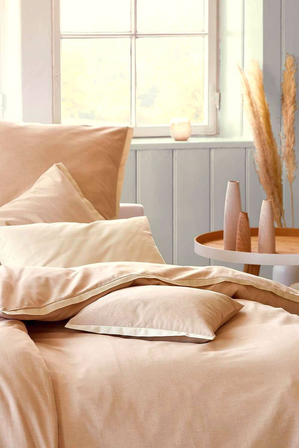 ungefärbte Bettwäsche aus bio Baumwolle (kbA) in Bett mit großem Fenster dahinter und dekoriertem Nachttische daneben