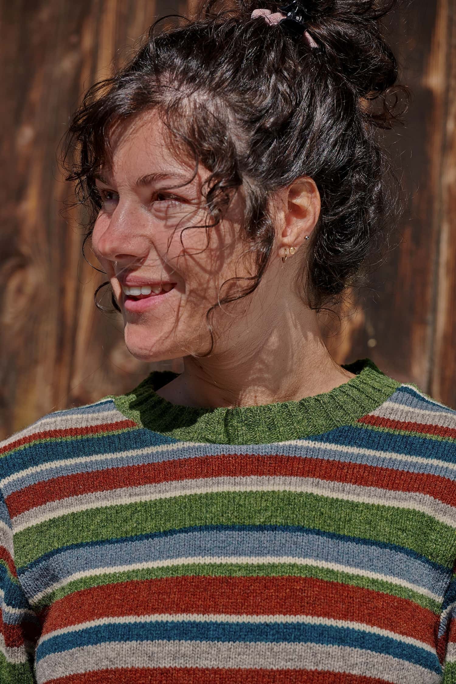 Portraitaufnahme von Frau mit dunklen Locken, die einen bunt gestreiften Wollpullover vom Finkhof aus Bio-Wolle trägt