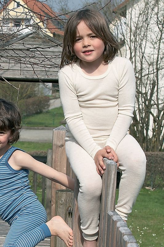Wollhemd Langarm naturweiß Mädchen trägt naturweißes langarm Wollhemd aus bio Wolle (kbT) , mit passender Hose und sitzt auf Klettergerüst
