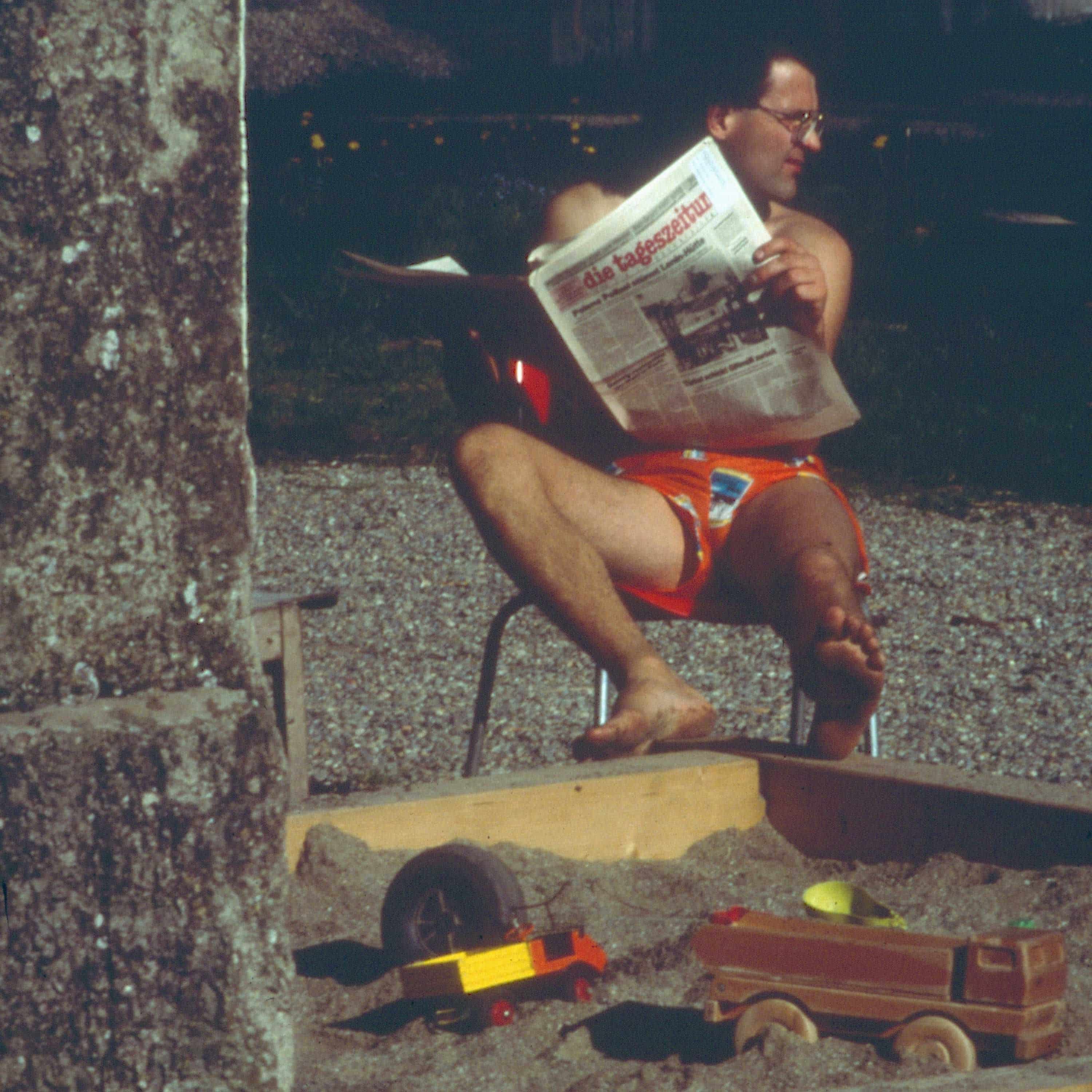 Finkhöfler sitzt neben Sandkasten und liest eine Zeitung