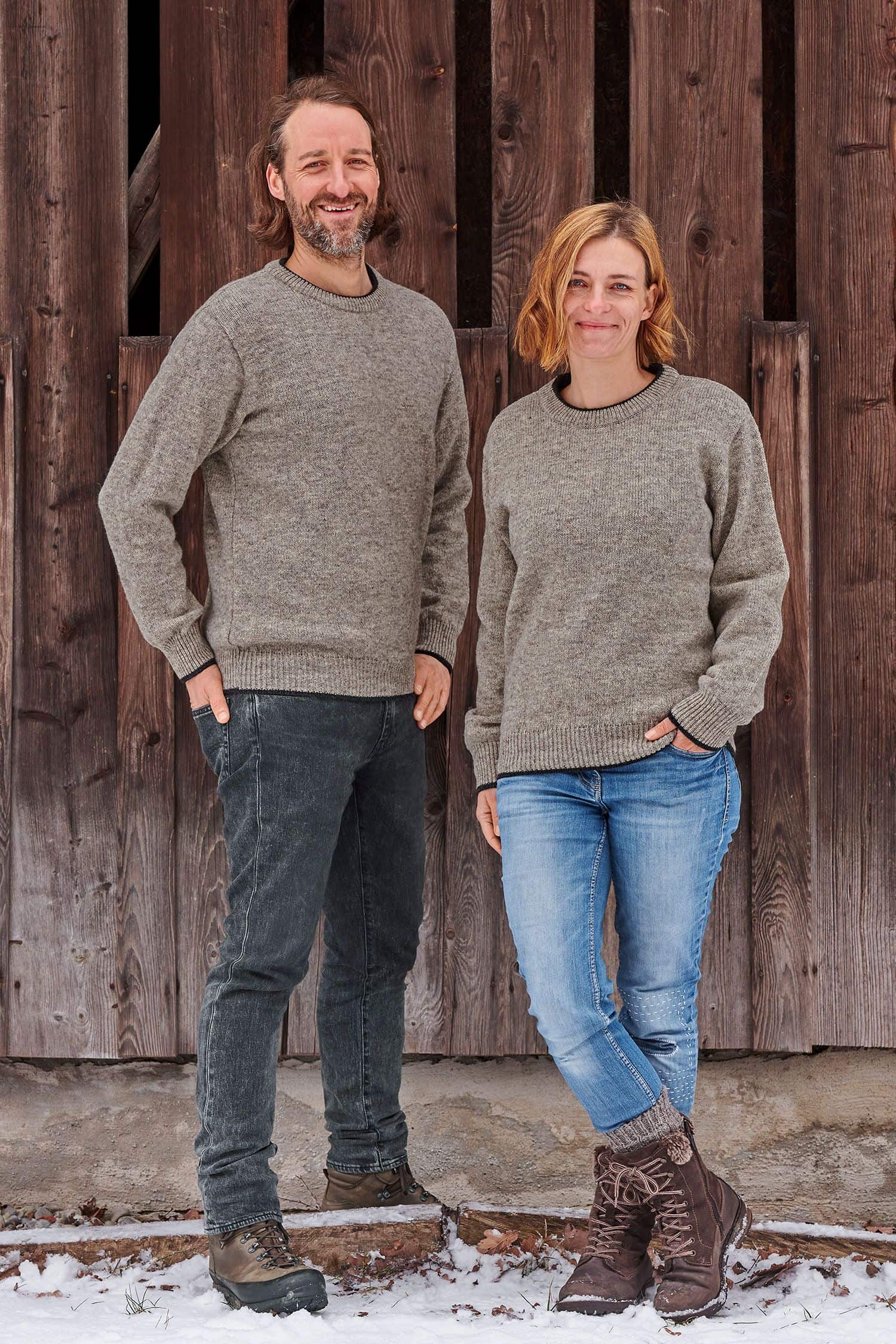 Finkhof-Pulli grau Gr. M Mann und Frau vor Holzfassade mit grauen Finkhof Pullis aus bio Wolle (kbT)