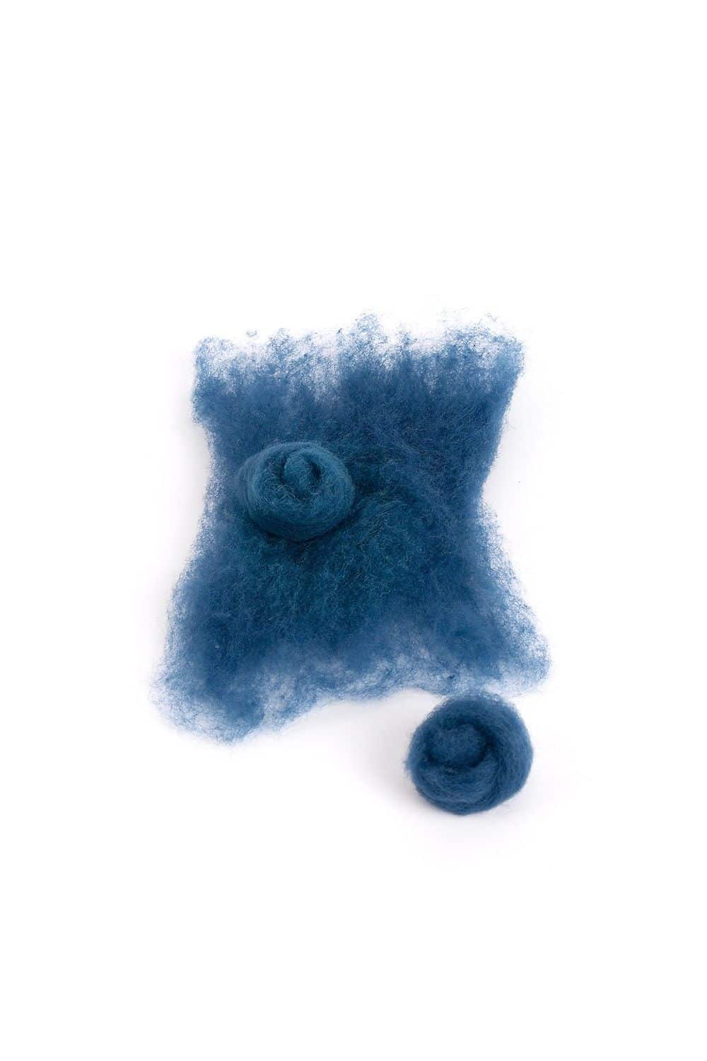 Stück lose blaue Finkhof Märchenwolle aus bio Merinowolle (kbT) und blaue Filzkugeln auf weißem Untergrund