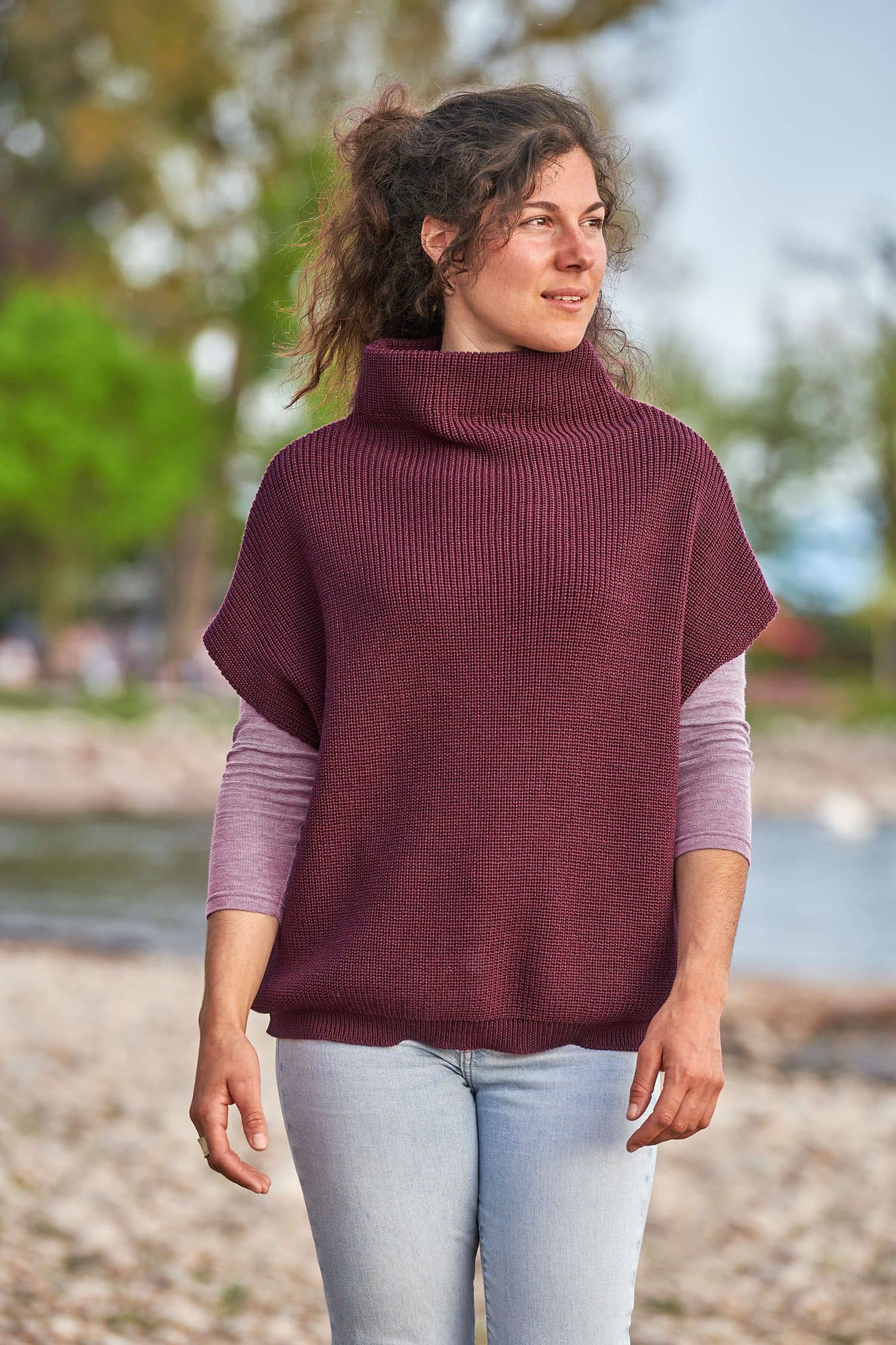 Frau trägt einen burgunderroten Strickpullunder aus bio Wolle (kbT) vom Finkhof mit einem lila Shirt und Jeans
