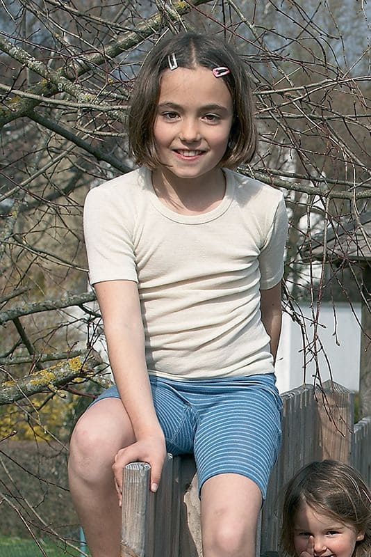 Wollhemd Kurzarm naturweiß Mädchen trägt naturweißes kurzarm Wollunterhemd aus bio Wolle (kbT)mit blauer kurzer Ringelhose, sitzend