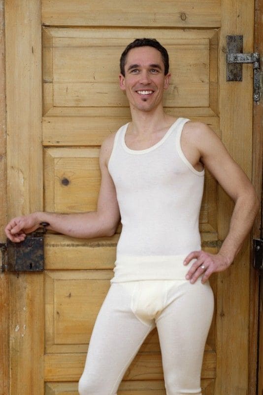 Mann lehnt an Tür und trägt eine lange Unterhose und ein naturweißes Trägerhemd aus bio Wolle (kbT) und Seide