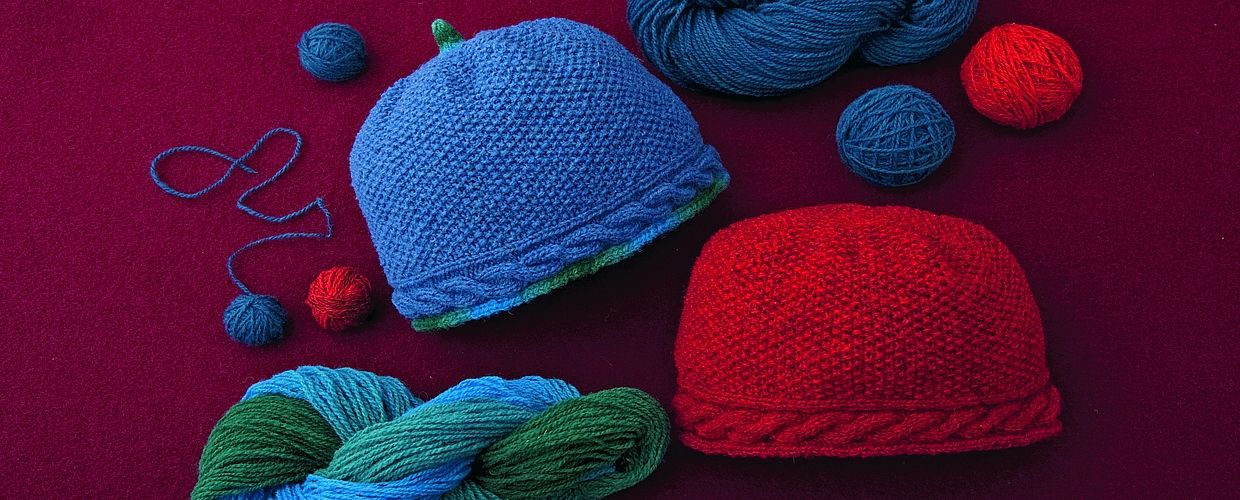 blaue und rote Strickmütze mit Wollknäulen auf beerefarbenem Untergrund für Strickanleitung