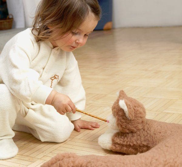 schlafanzug-wolle5cee3be05a3bb Kind mit naturweißem Einteilerschlafanzug aus bio Wolle (kbT) mit Schafgrafik und füttert Plüschkatze mit Salzstange