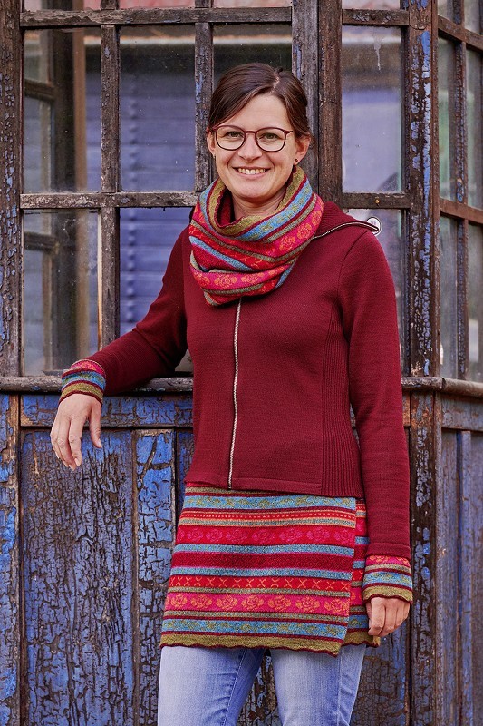 Frau trägt rote Weste mit Zipper, bunt rot gemusterten ,,Konfetti" Armstulpen, Cacheur und Loopschal aus bio Wolle (kbT)