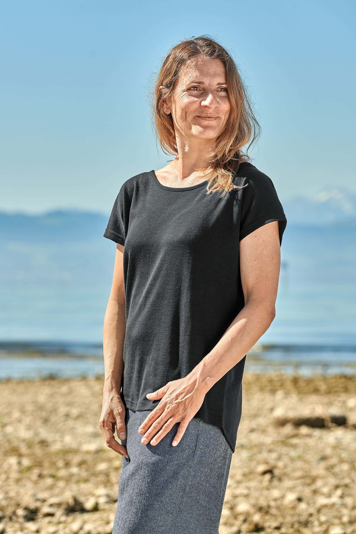 Seitliche Aufnahme von Frau am Bodensee, die ein schwarzes Oversize Shirt aus Bio-Wolle und Seide trägt