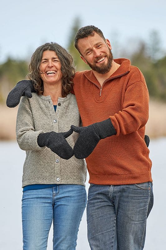 Mann und Frau mit Strickpullis tragen graue Fäustlinge aus bio Wolle (kbT) vom Finkhof und formen damit ein Herz