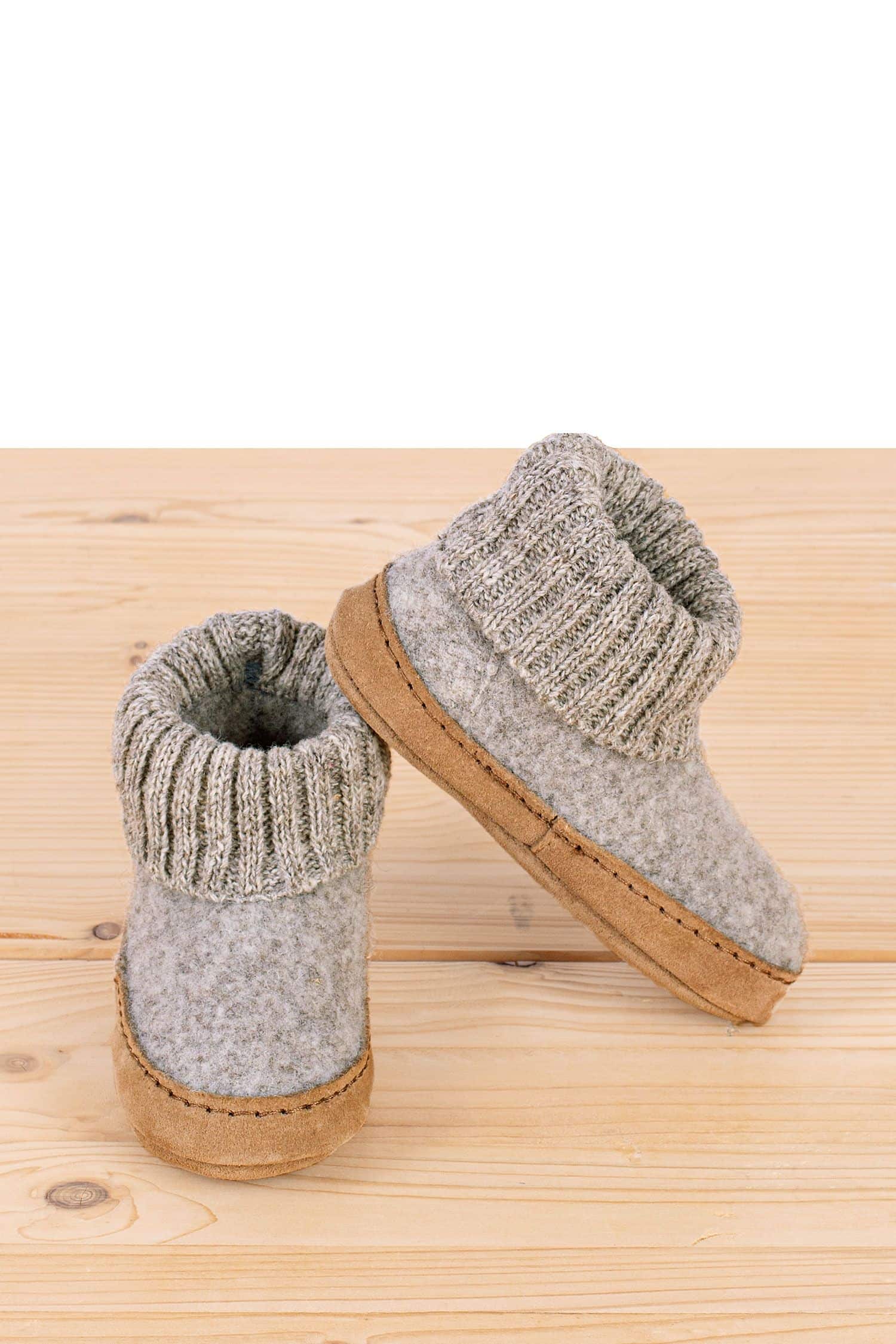 hellgraue Kinderhüttenschuhe vom Finkhof aus bio Wolle (kbT) und pflanzlich gegerbtem Leder stehen auf Holzboden