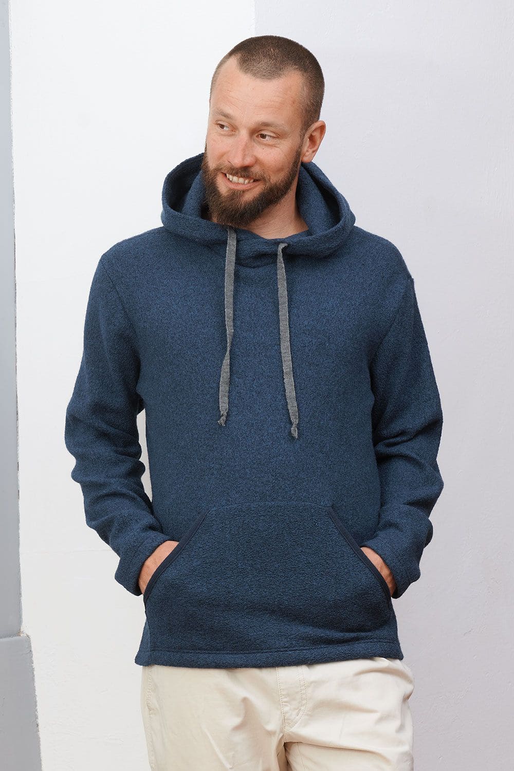 Mann lehnt an Wand und trägt marineblauen Kapuzenpulli aus bio Wolle (kbT) mit beiger Jeans