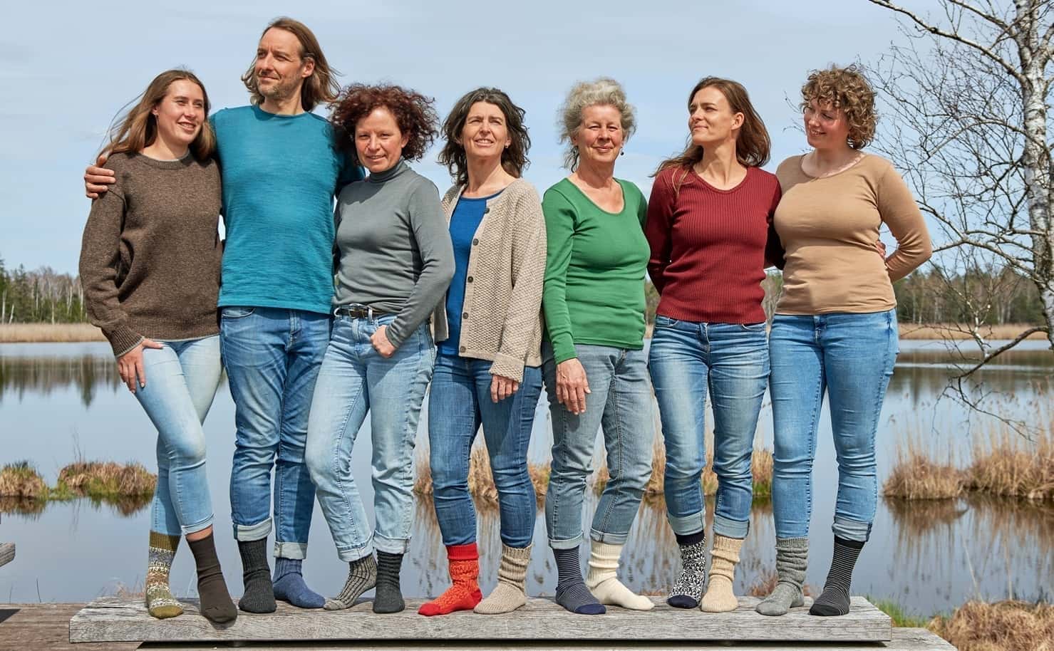 Gruppenfoto auf einem Steg, Menschen tragen unifarbige Shirts in verschiedenen Farben, Jeans und Wollsocken