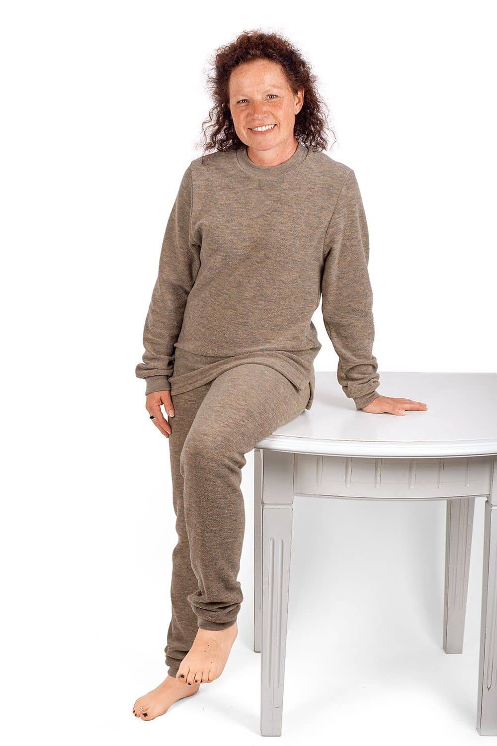 Frau sitzt auf Holztisch und trägt einen walnussbraunen Wollfrotte-Schlafanzüge aus bio Wolle (kbT)