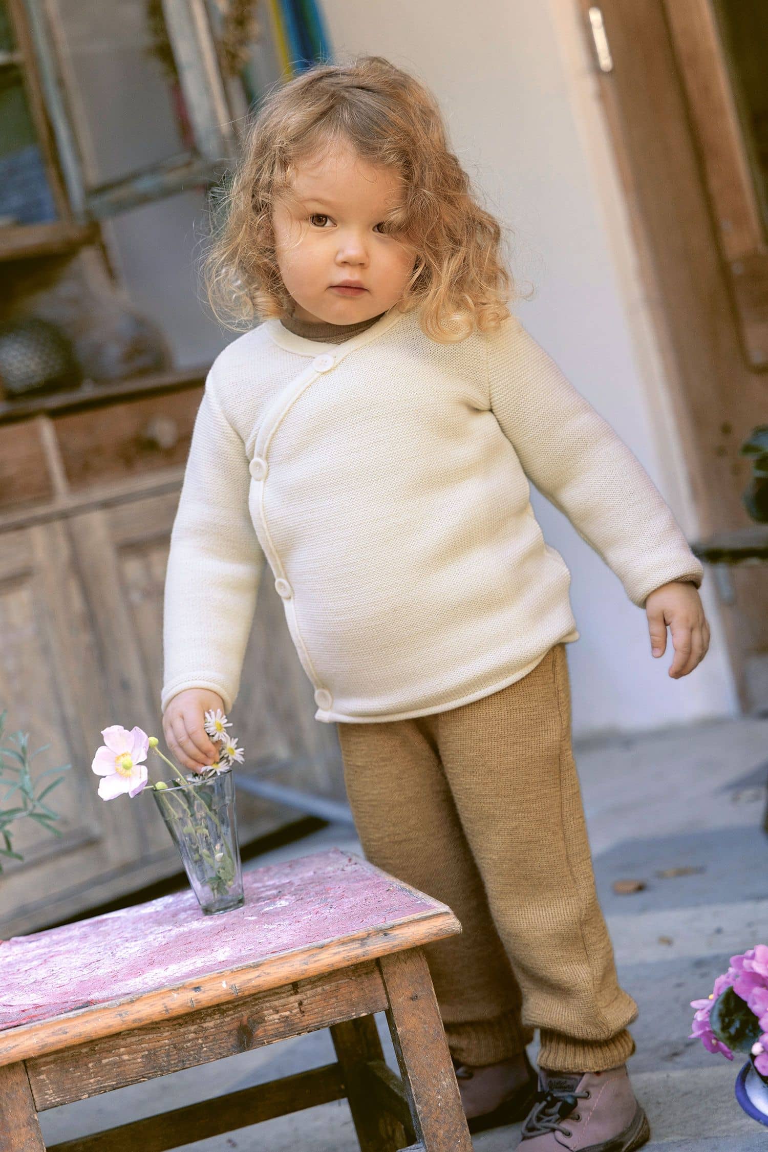 Kind mit weißem Pullover trägt eine hellbraune Hose aus bio Wolle (kbT)