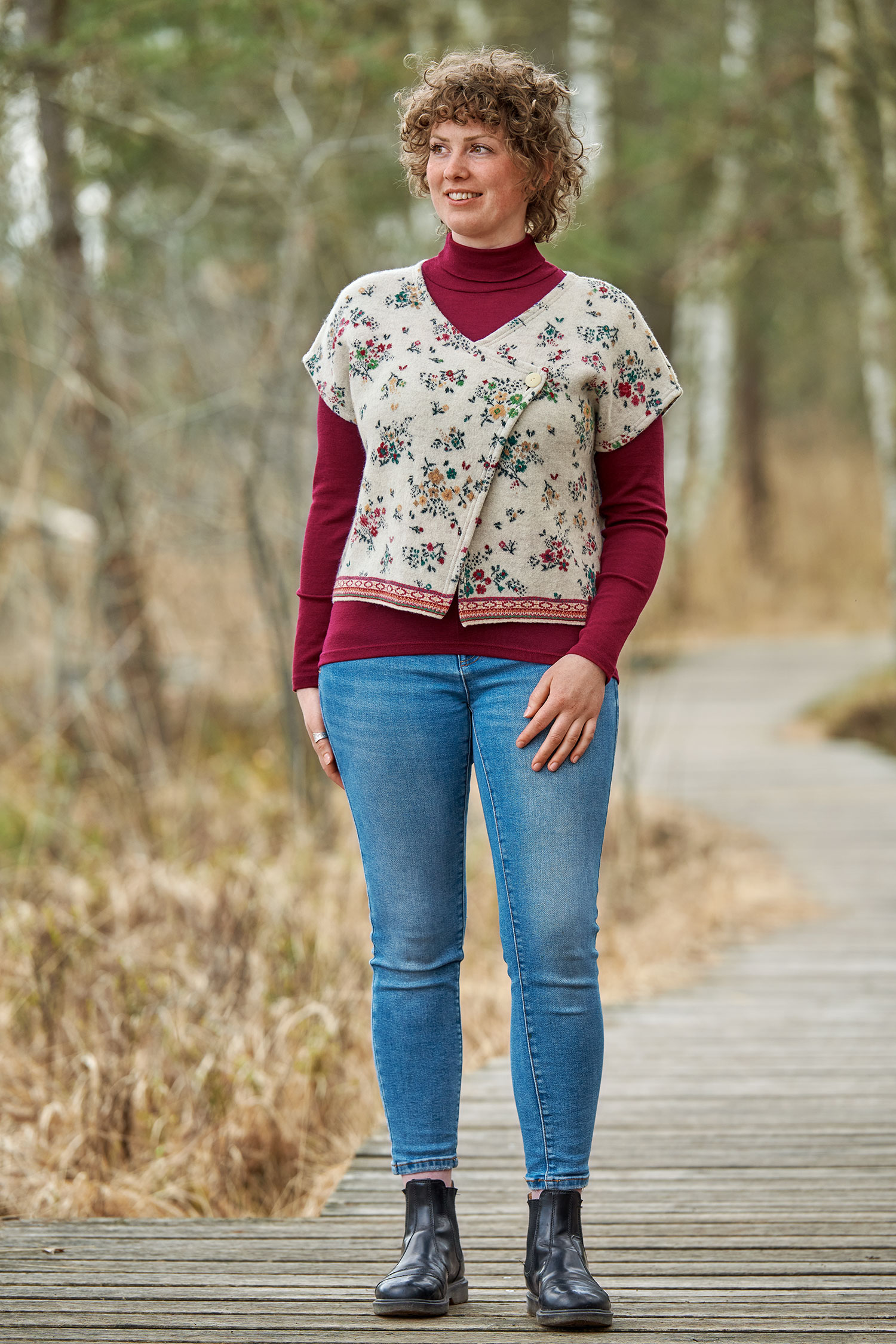 Frau mit rotem Shirt trägt Walk Kurzweste in naturweiß mit floralem Muster aus bio Merinowolle (kbT) und Baumwolle (kbA)