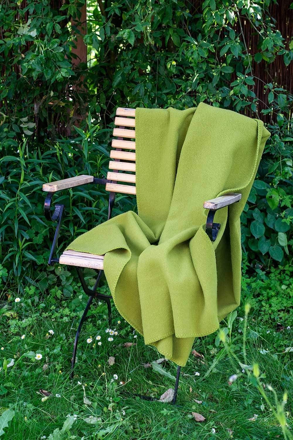 grüne Wolldecke aus bio Wolle (kbT) vom Finkhof über Stuhl gelegt auf einer Wiese