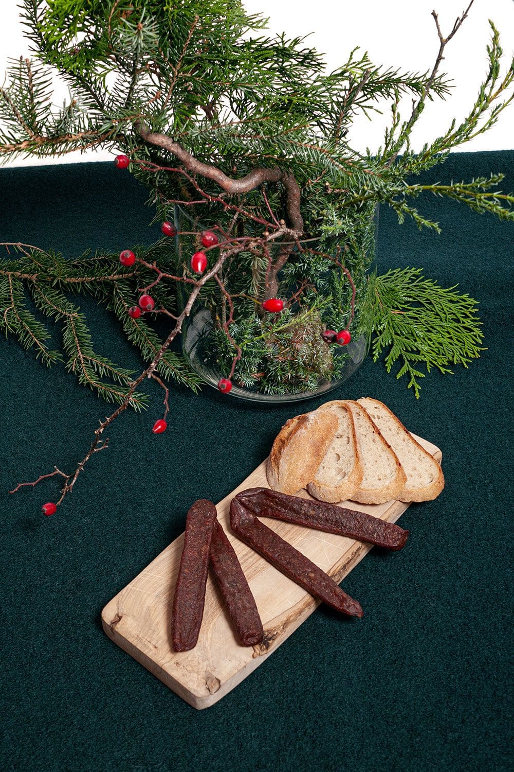 Bio-Lammjäger Finkhof Lammjäger auf Brettchen mit Brotscheiben, grauem Untergrund und Vase mit winterlichen Ästen